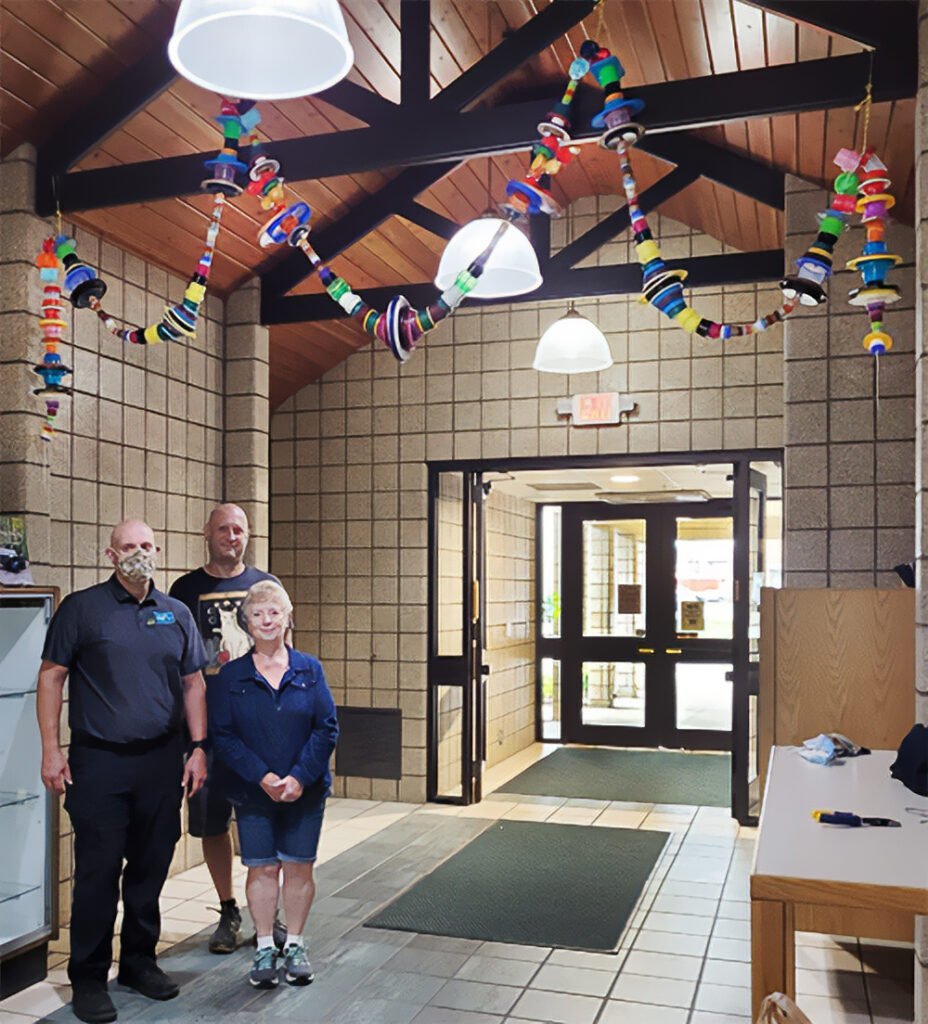 3 people show off their garland they made with bottle caps
